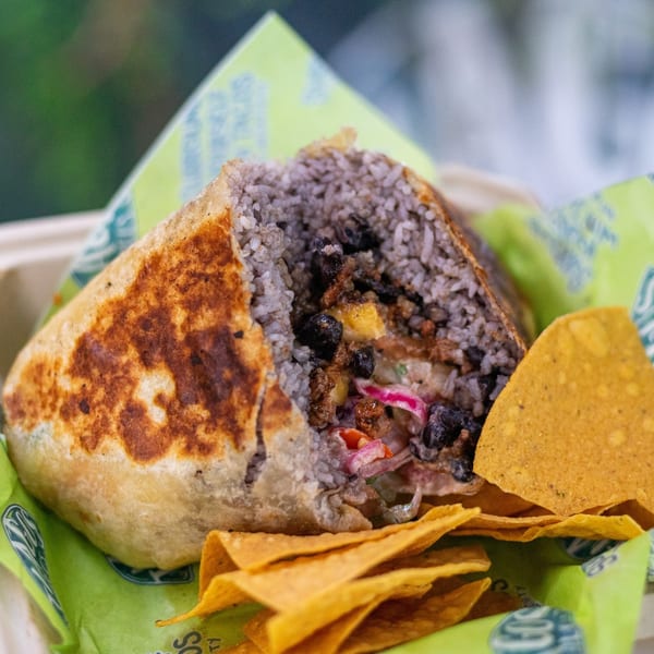 A Tiagos Tacos burrito, cut open to show rice, beans, and other fillings, with tortilla chips.