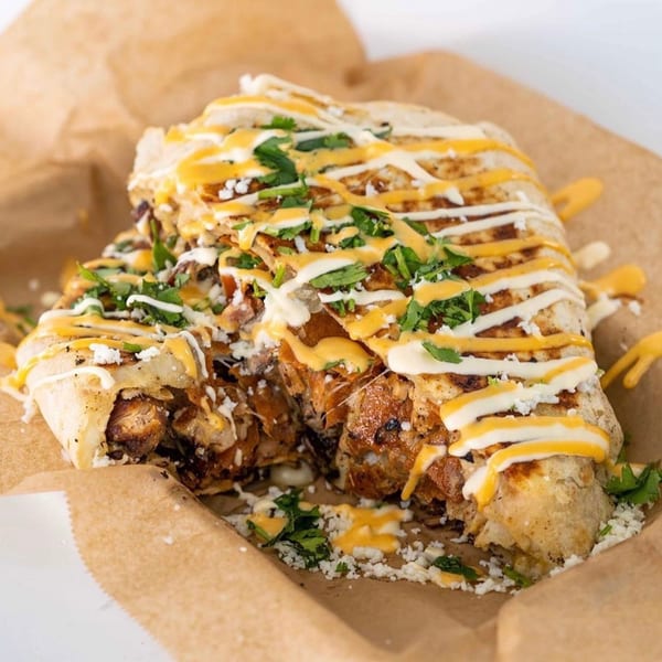 A large, cut Tiagos Tacos burrito with chicken, cheese, and sauce, served in a paper tray.