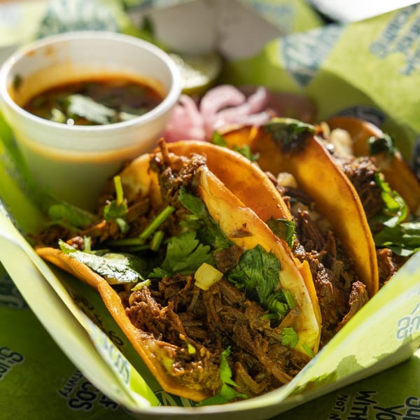 Three Tiagos Tacos with shredded meat and cilantro, served with a side of dipping sauce.