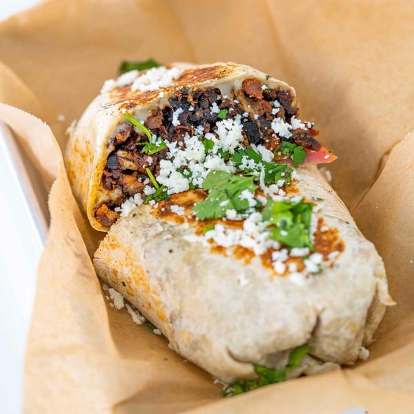 A Tiagos Tacos burrito, cut in half, revealing a savory filling of meat, beans, cheese, and cilantro.