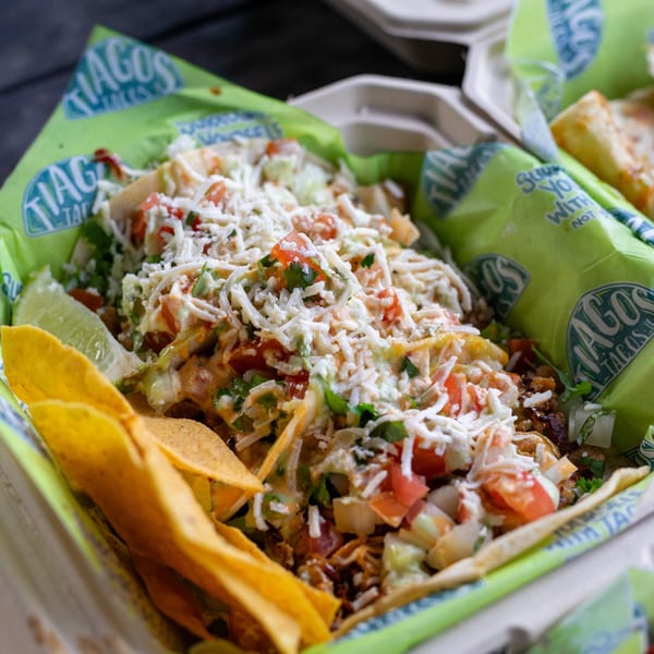 Tiagos Tacos' loaded tacos with shredded cheese, pico de gallo, and a lime wedge in a takeout container.