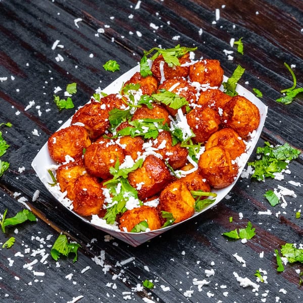 Tiagos Tacos' golden-brown fried cheese curds, topped with crumbled white cheese and fresh cilantro, on a dark wooden surface.