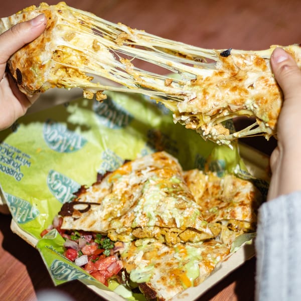 Hands pulling apart a cheesy quesadilla, revealing long strings of melted cheese and fillings.
