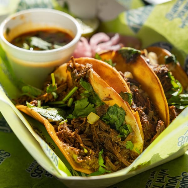 Three Tiagos Tacos birria tacos with cilantro and onions, served with a side of consommé.