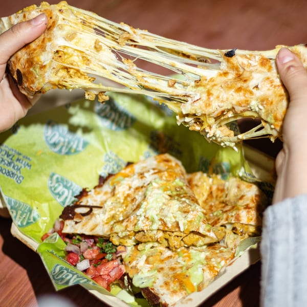 Hands pulling apart a cheesy quesadilla from Tiagos Tacos, revealing melted cheese strings and fillings.