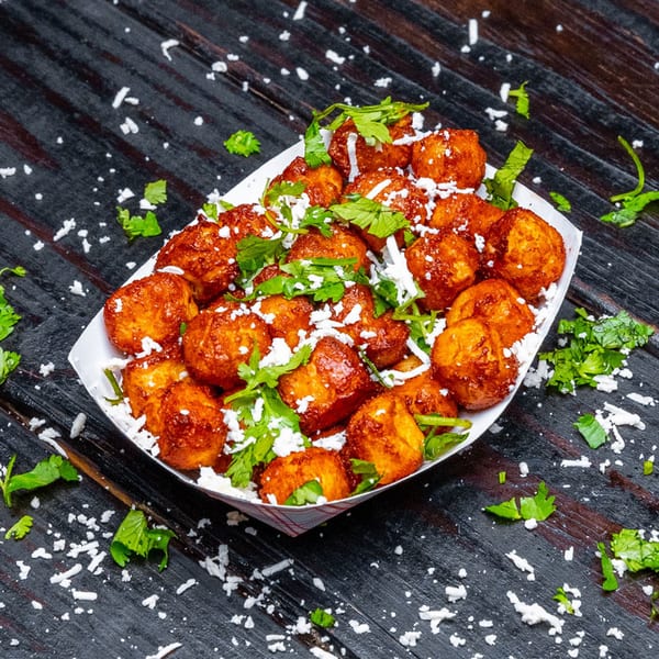 Tiagos Tacos' golden-brown fried cheese curds, topped with crumbled white cheese and fresh cilantro, on a dark wooden surface.