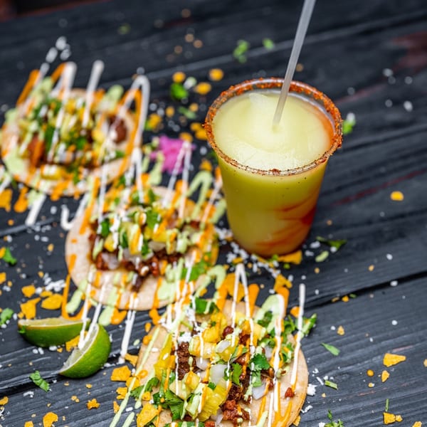 Three Tiagos Tacos with various toppings and sauces, next to a frozen margarita with a chili-lime rim.
