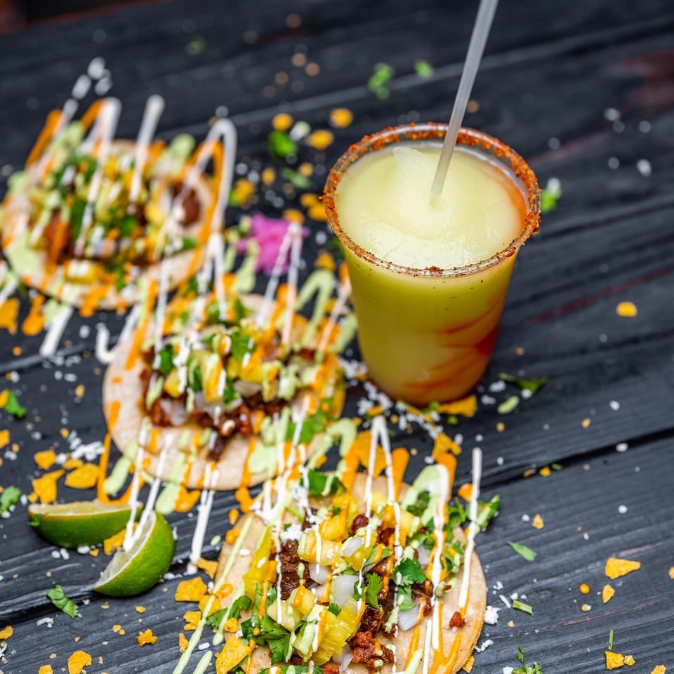 Three Tiagos Tacos with various toppings and sauces, next to a frozen margarita with a chili-lime rim.