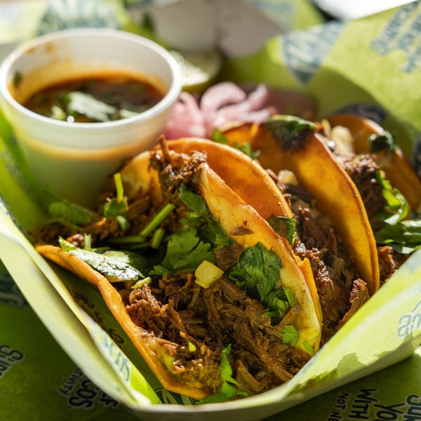 Three Tiagos Tacos birria tacos with cilantro and onions, served with a side of consommé.